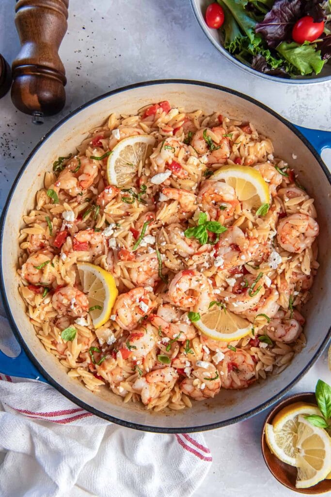 Shrimp orzo pasta with lemon slices in a skillet.
