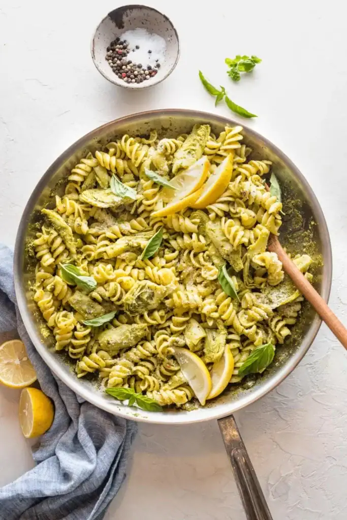Pesto pasta with artichoke hearts and lemon in a pot.