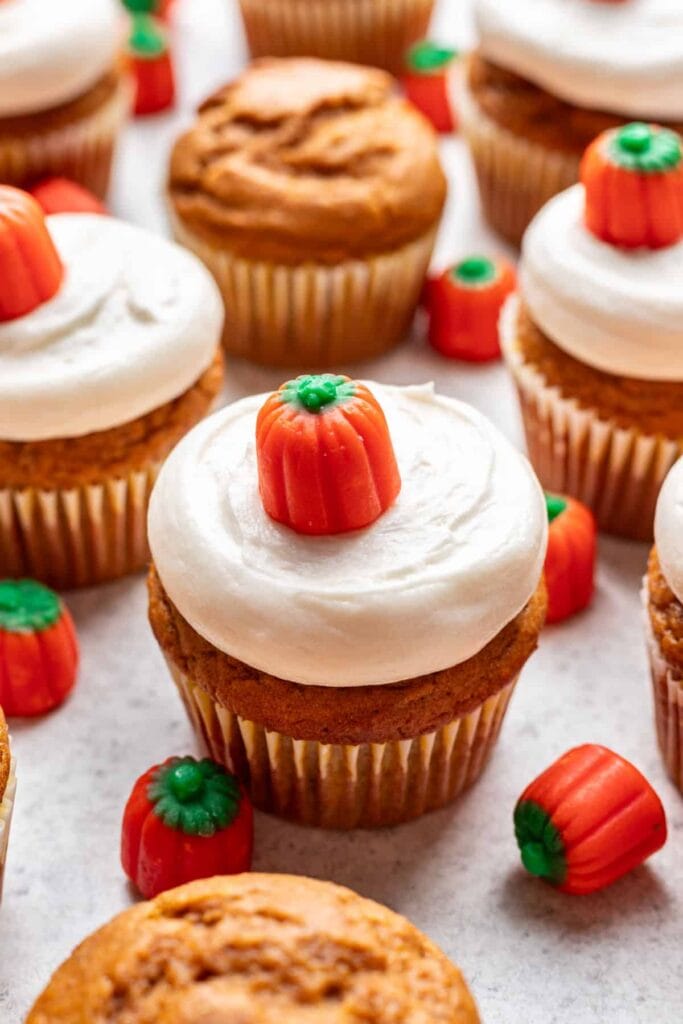 Pumpkin cupcakes with cream cheese frosting on parchment paper.