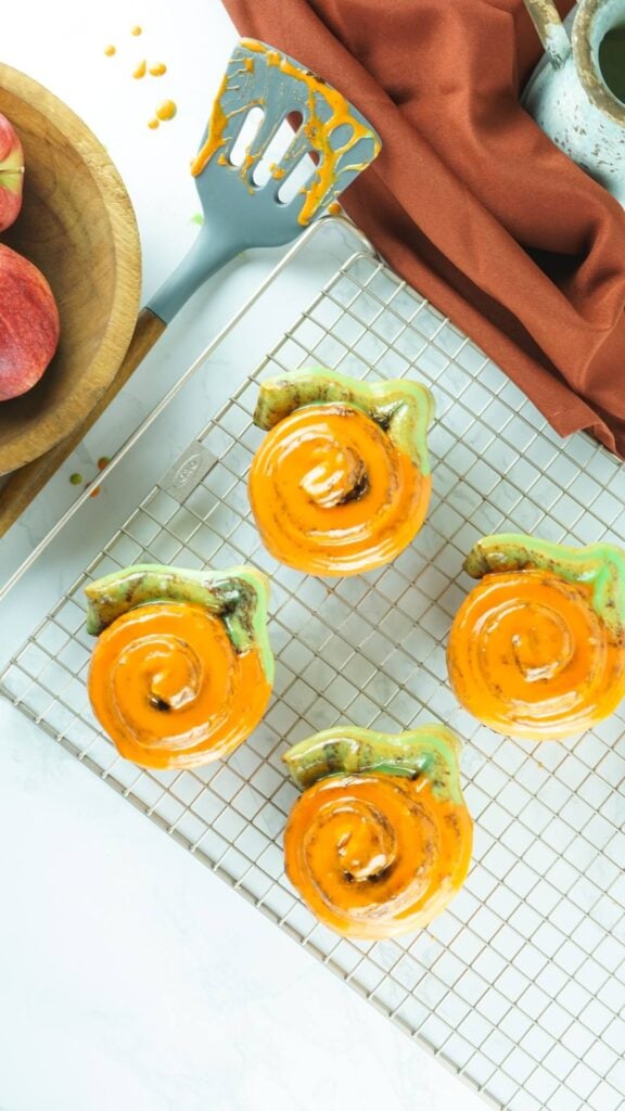 Pumpkin-shaped cinnamon rolls on a cooling rack.