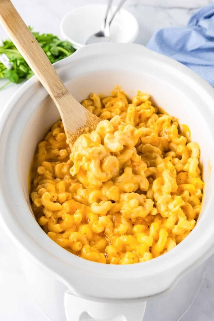 Mac and cheese in a slow cooker with a wooden spoon.