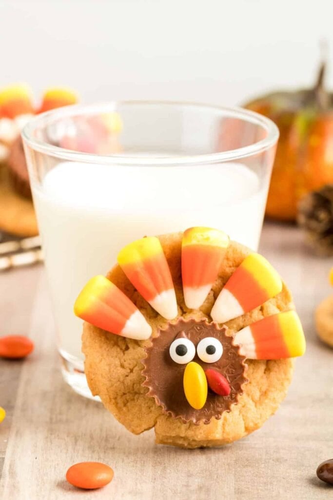 Thanksgiving turkey cookie in front of a glass of milk.