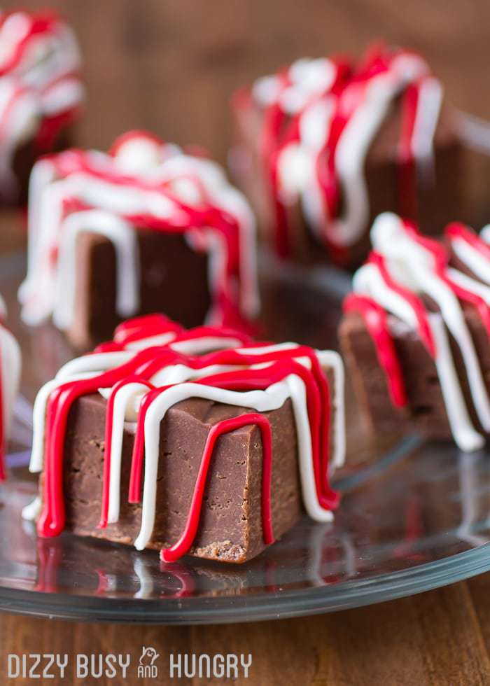 Chocolate fudge cubes drizzled with red and white icing, arranged on a glass plate over a wooden surface.