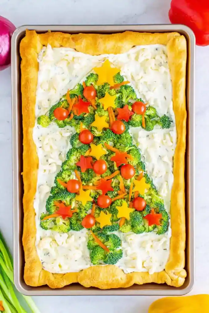 Sheet pan crescent crust topped with creamy spread, broccoli florets shaped as a Christmas tree, decorated with cherry tomatoes and bell pepper stars.