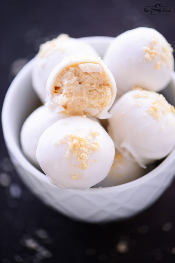 Eggnog truffles coated in white chocolate in a bowl, one cut open.