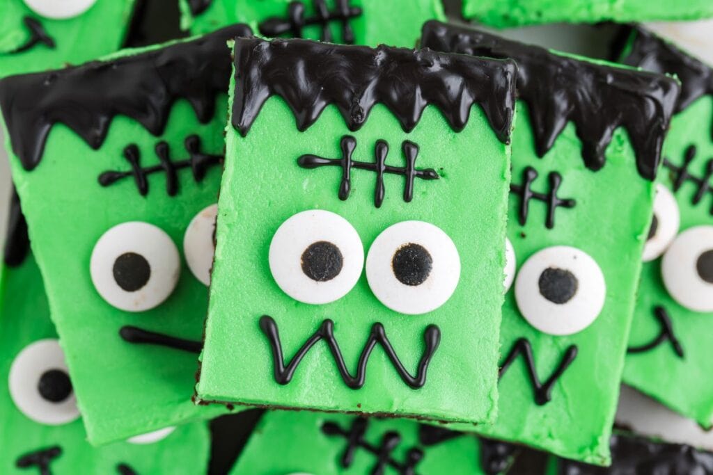 Green Halloween dessert bars decorated like Frankenstein faces with black icing hair, candy eyes, and stitched details, arranged close together.