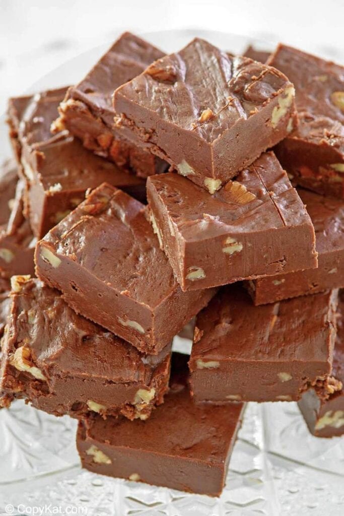 Chocolate fudge squares with embedded nuts, stacked on a clear glass plate.