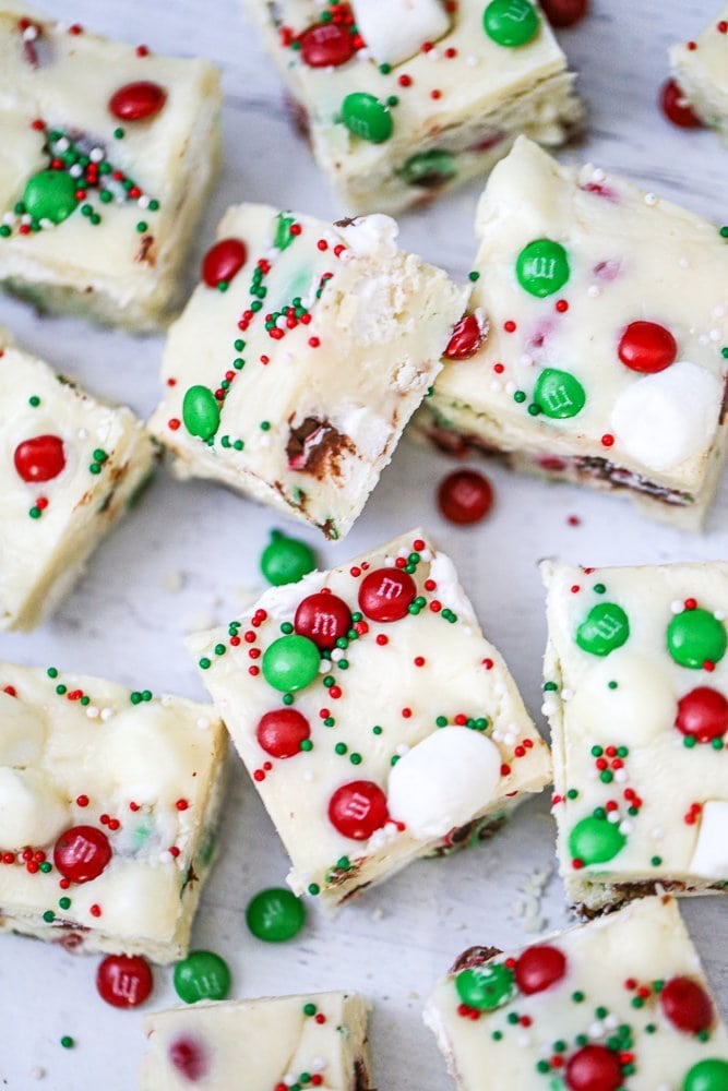 White chocolate fudge squares topped with red and green candies and sprinkles, arranged on a light surface for a holiday look.