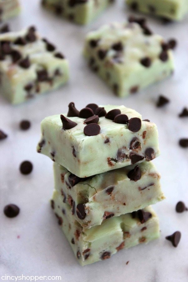 Light green mint fudge squares with chocolate chips, stacked in the foreground with scattered chips on a pale surface.