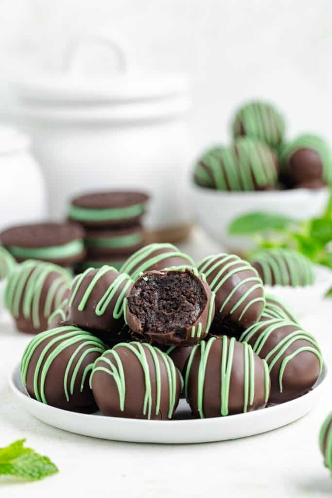 Chocolate-coated mint Oreo truffles drizzled with green chocolate, arranged on a plate with one truffle cut open to reveal the rich Oreo filling.