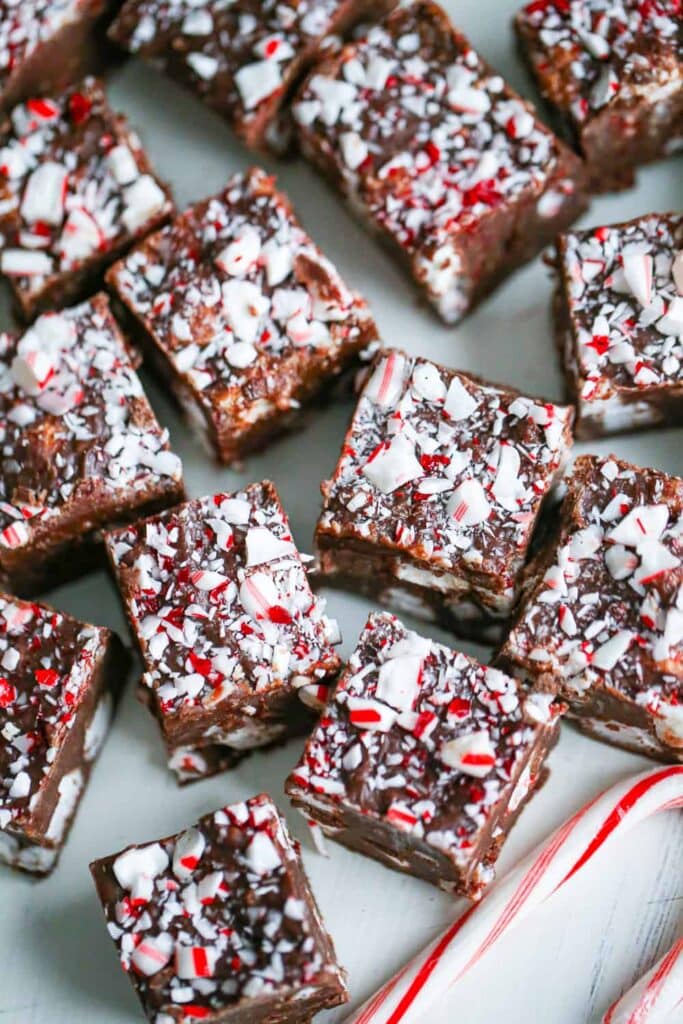 Chocolate fudge squares topped with crushed peppermint, arranged on a light surface with a candy cane nearby.