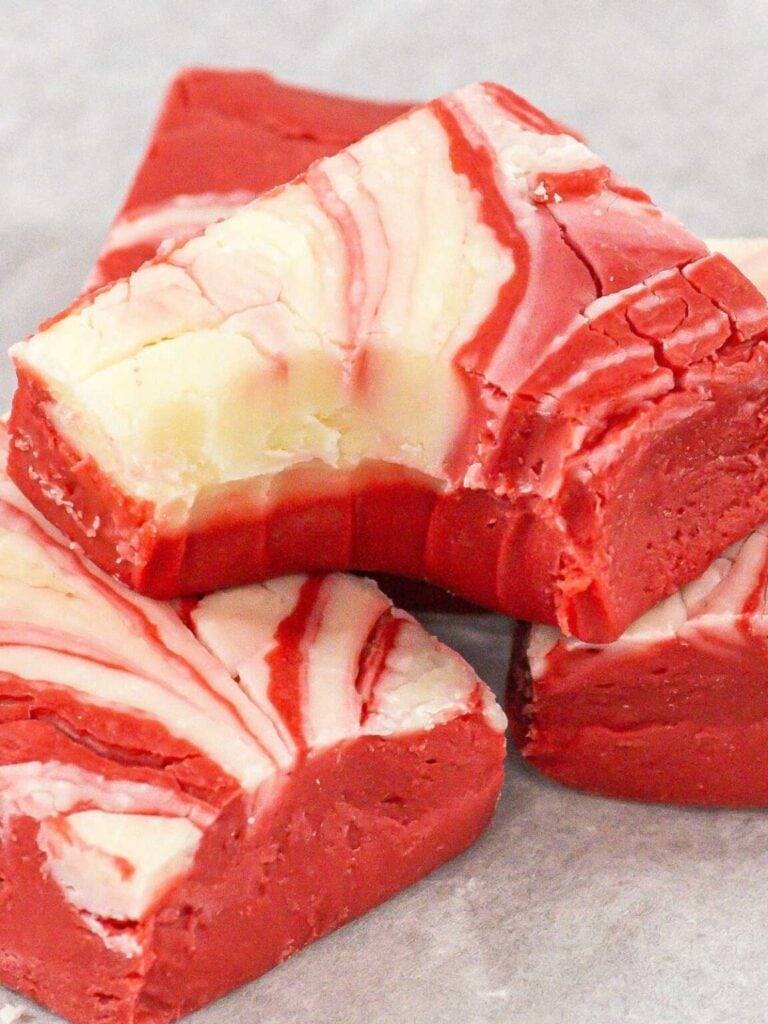 Red and white swirled fudge squares stacked on a light surface, showing smooth marbled layers with festive contrast.