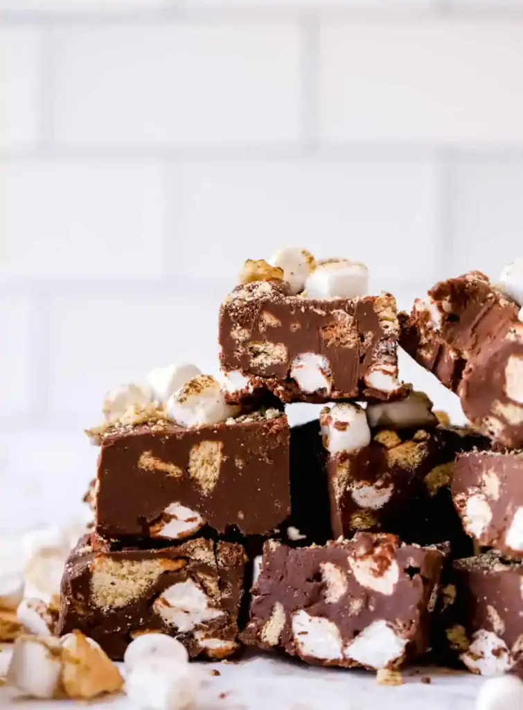 Chocolate fudge squares with graham cracker chunks and marshmallows, stacked on a white tiled surface.