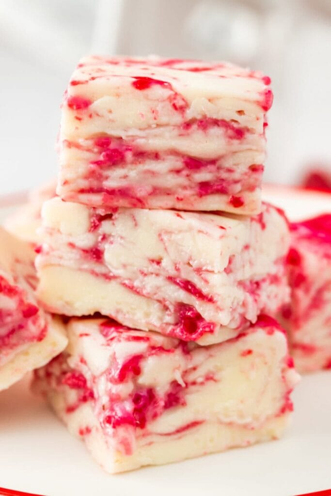White chocolate fudge with vibrant raspberry swirls, stacked to show marbled texture and glossy finish.