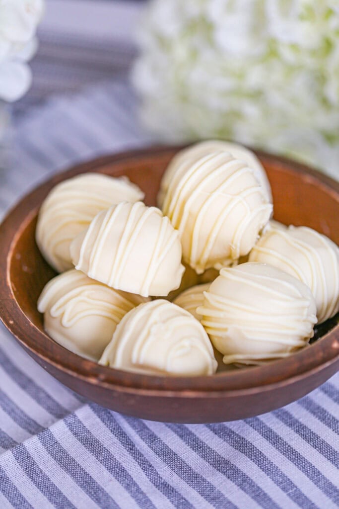 White chocolate truffles drizzled with white chocolate, arranged in a wooden bowl on a striped cloth.