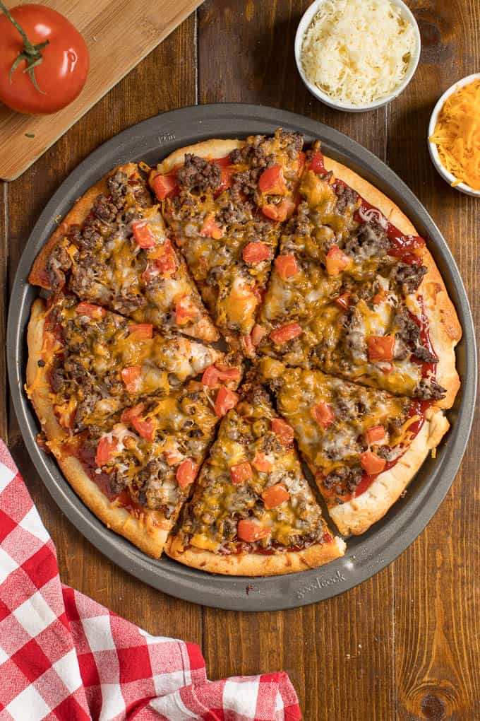 Overhead view of cheeseburger pizza on a wooden table.