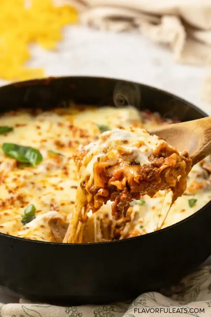 Cheesy lasagna skillet with a serving on a wooden spoon.