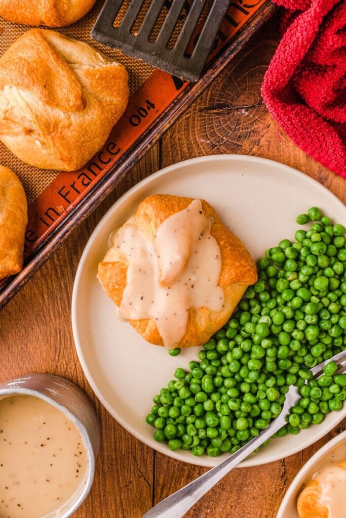 Chicken puffs on a plate with peas and gravy.