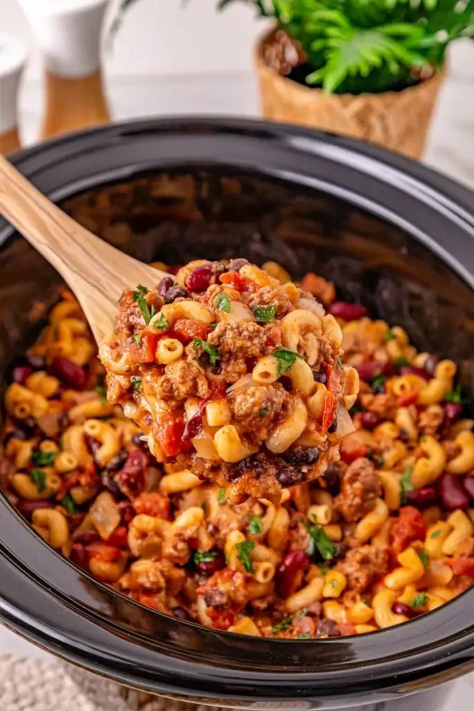 Crockpot chili mac in a slow cooker with a wooden spoon.