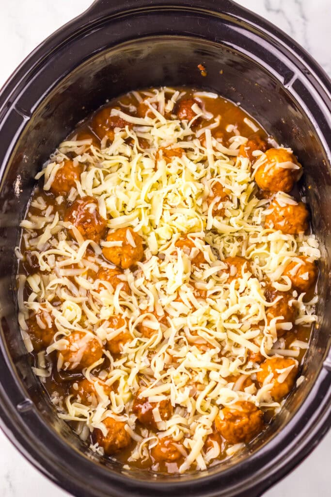 Shredded cheese over saucy meatballs in a slow cooker.