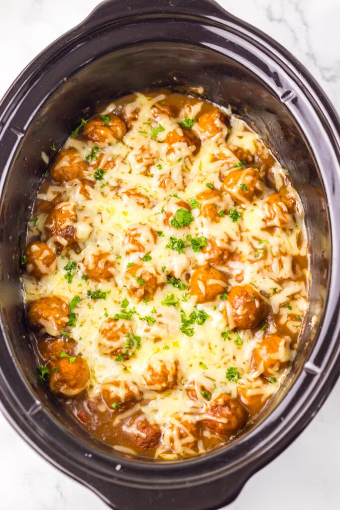 Melted cheese over saucy meatballs in a slow cooker.