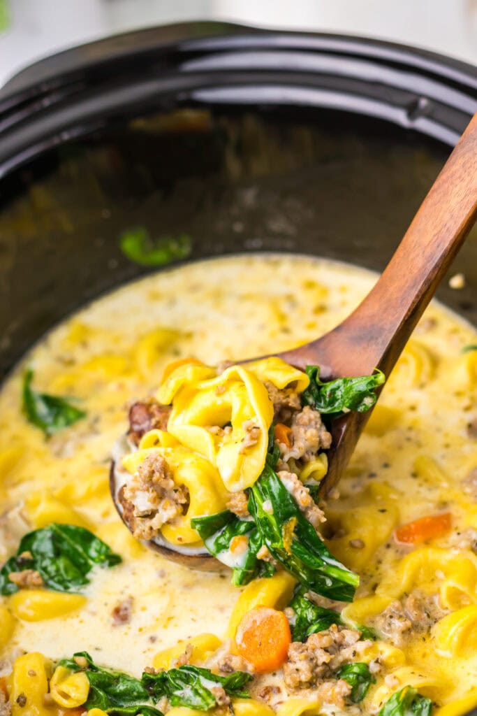 Crockpot tortellini soup on a wooden spoon.