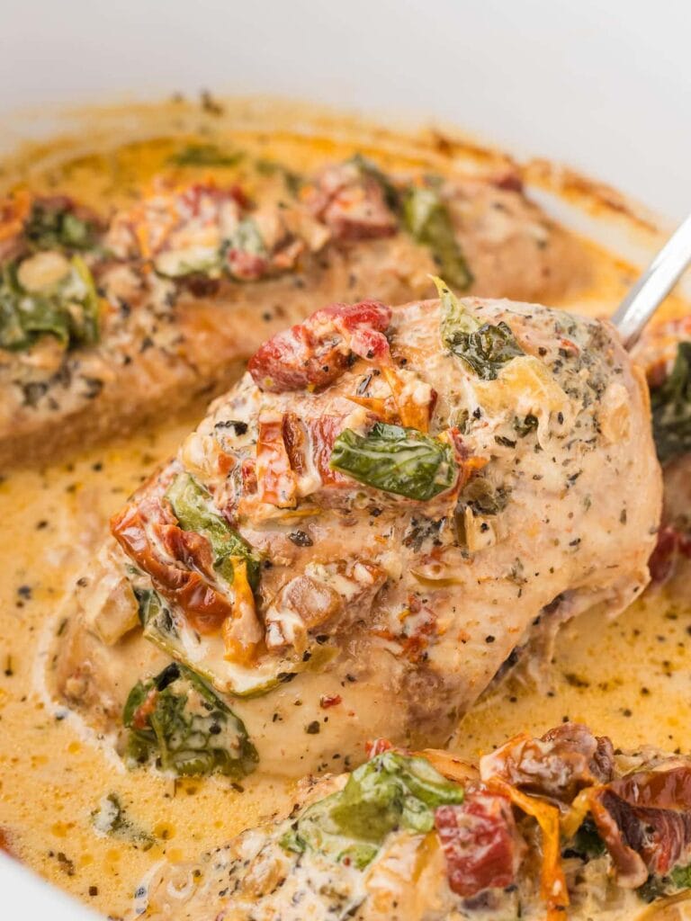 Crockpot Tuscan chicken on a serving spoon.
