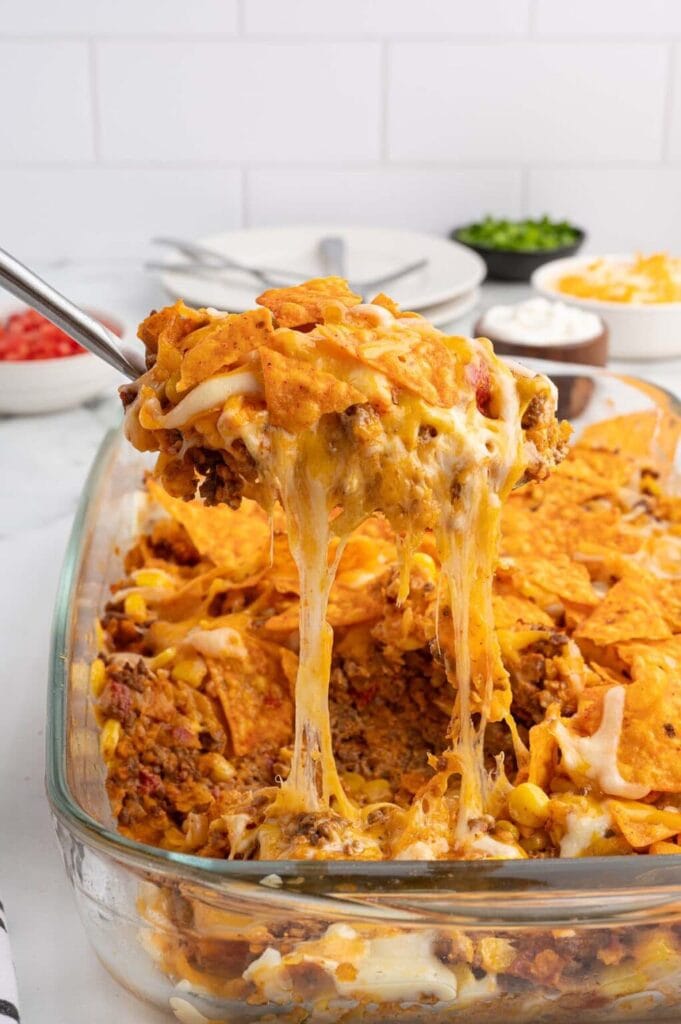 Dorito Casserole in a baking dish with a spoon lifting a cheesy serving.