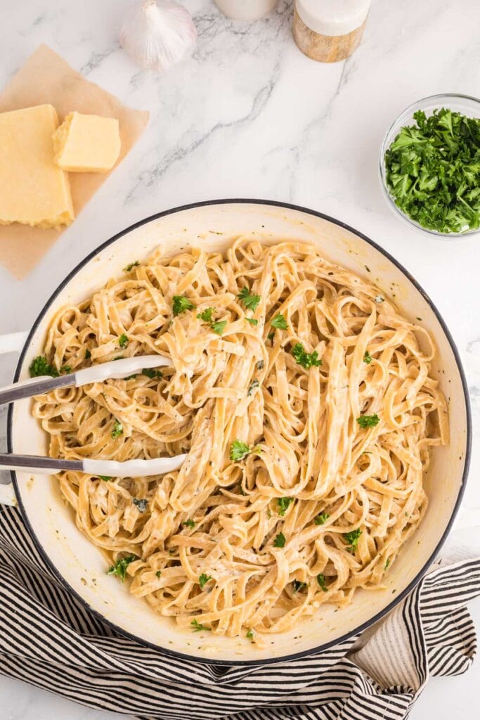 Fettuccine Alfredo in a skillet with serving tongs.