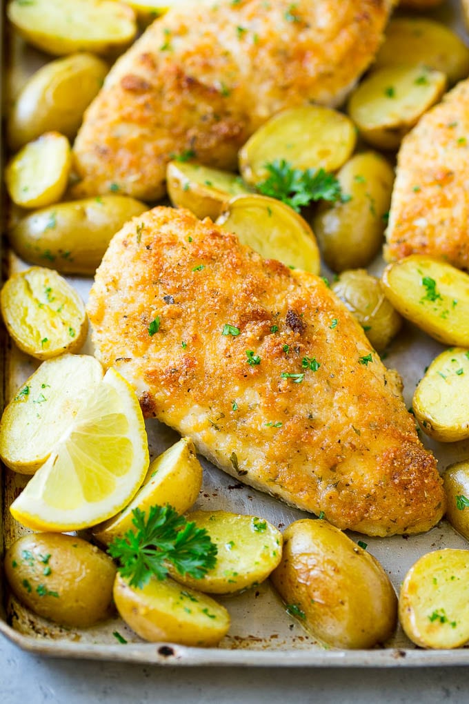 Italian Chicken with roasted baby potatoes and lemon wedges on a sheet pan.