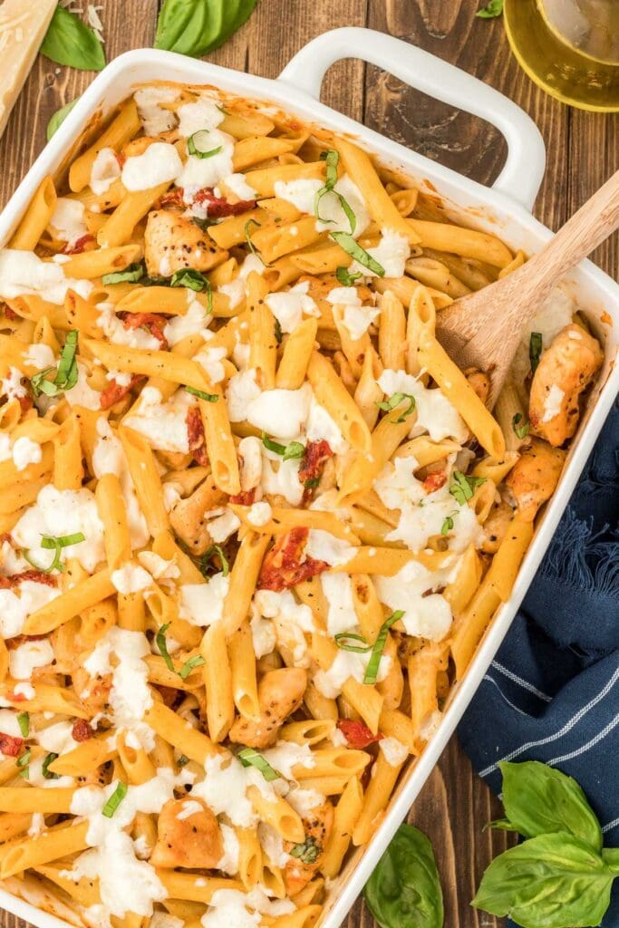 Marry Me chicken pasta casserole in a baking dish with a wooden spoon.