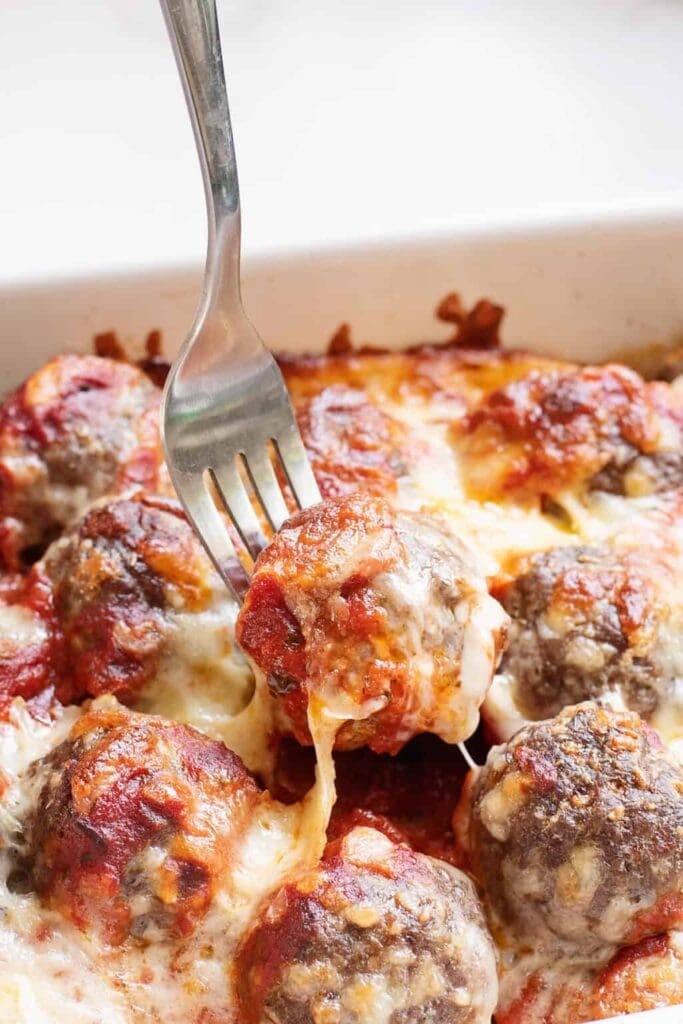 Close-up of meatball sub casserole with a fork lifting a cheesy meatball.