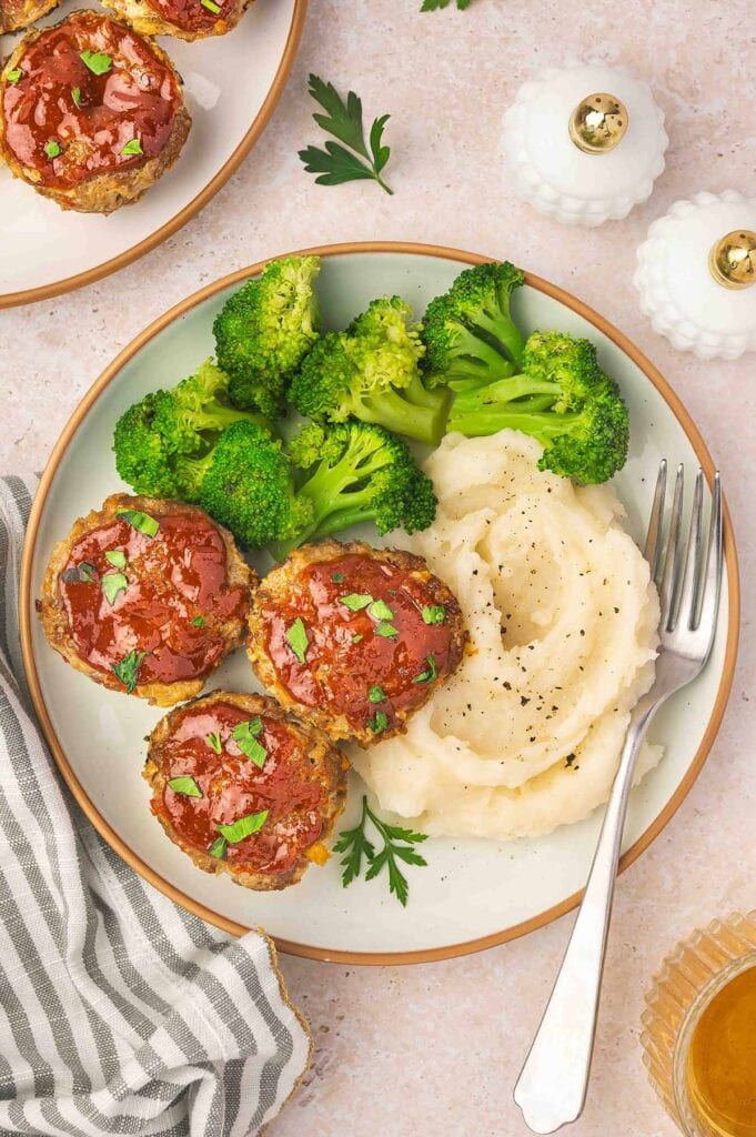 Mini meatloaf on a plate with mashed potatoes and broccoli.