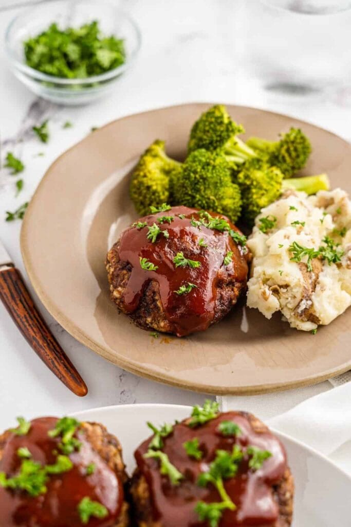 Mini meatloaves served on a plate with broccoli and mashed potatoes.