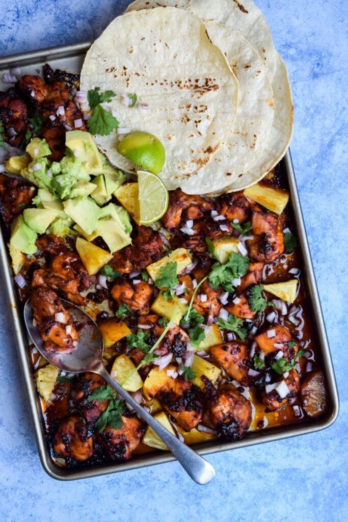 One Pan Chicken Pineapple Tacos on a sheet pan with tortillas, avocado, and lime.