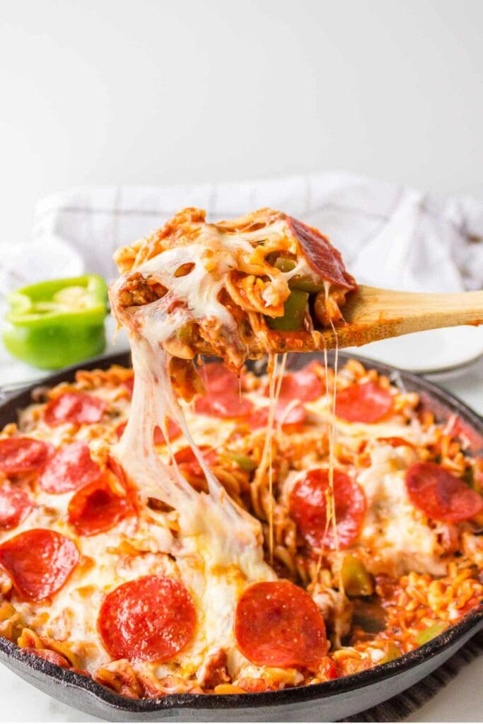 Pizza pasta in a skillet with a wooden serving spoon.