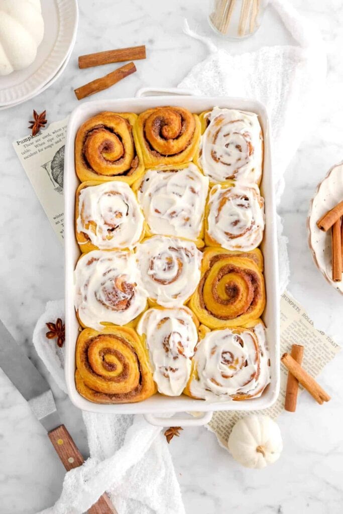 Pumpkin cinnamon rolls with vanilla cream cheese frosting in a baking dish.