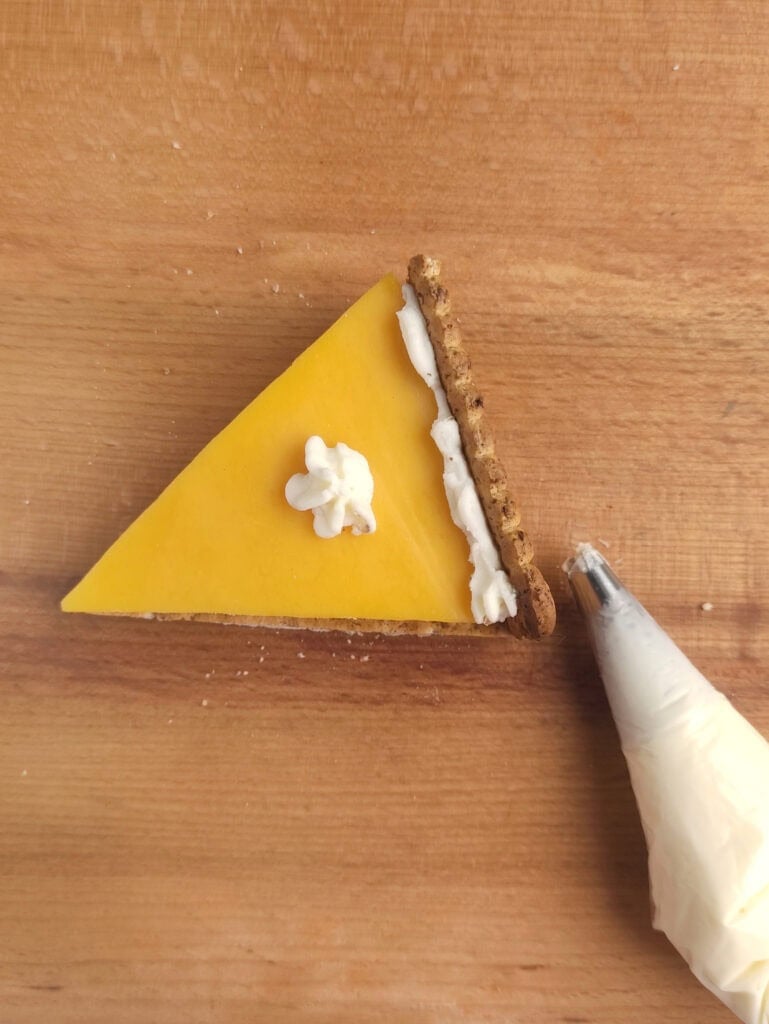 Finishing a cheese cracker with cream cheese.
