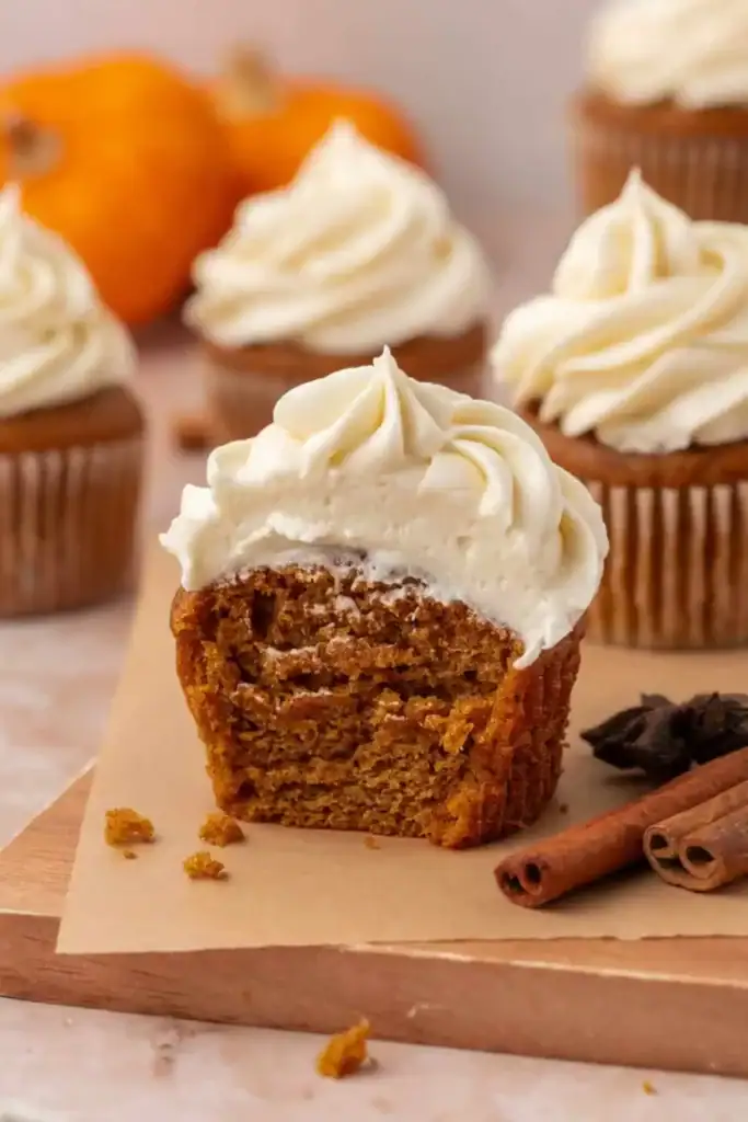 Pumpkin spice cupcakes with cream cheese frosting on a wooden board.