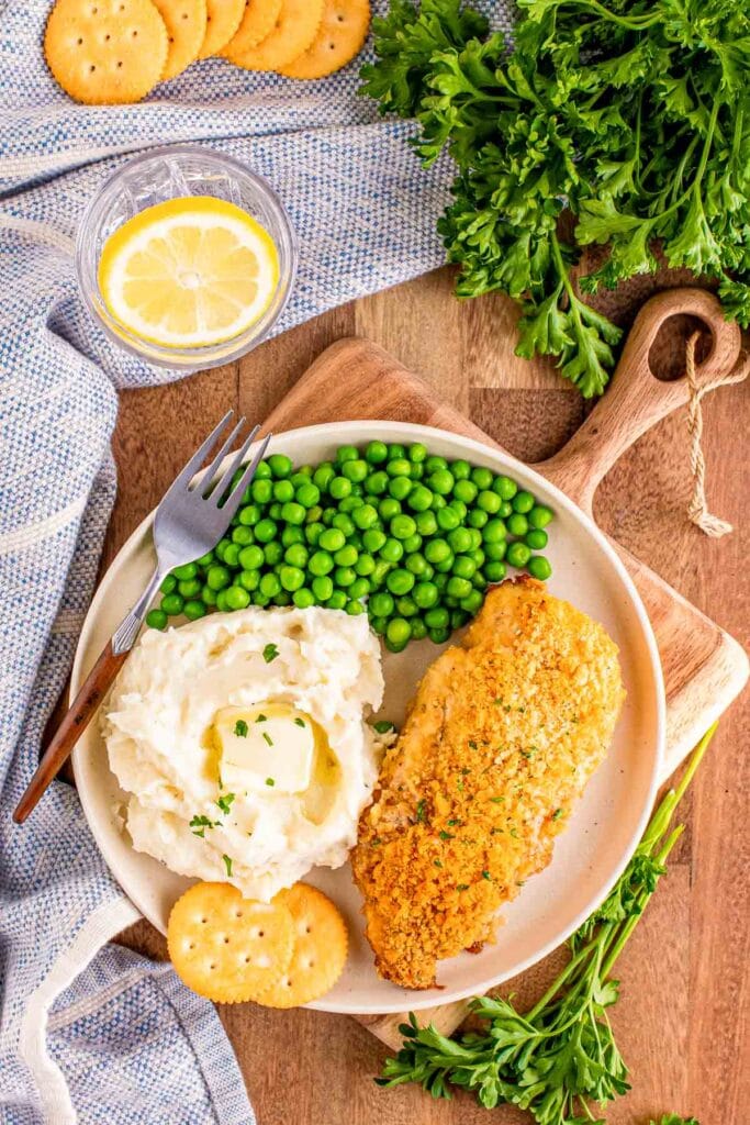 Ritz cracker chicken on a plate with mashed potatoes and peas.