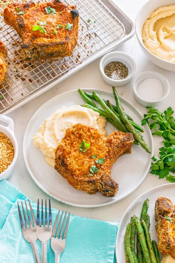 Shake and bake pork chops served on a plate with mashed potatoes and green beans.