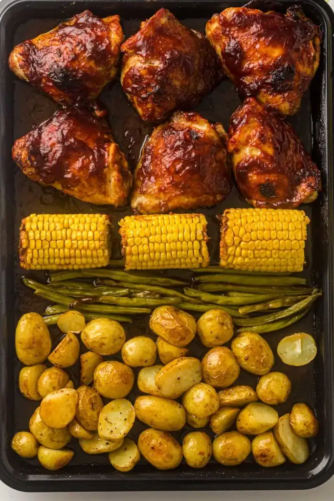 BBQ chicken with roasted potatoes, green beans, and corn on a sheet pan.