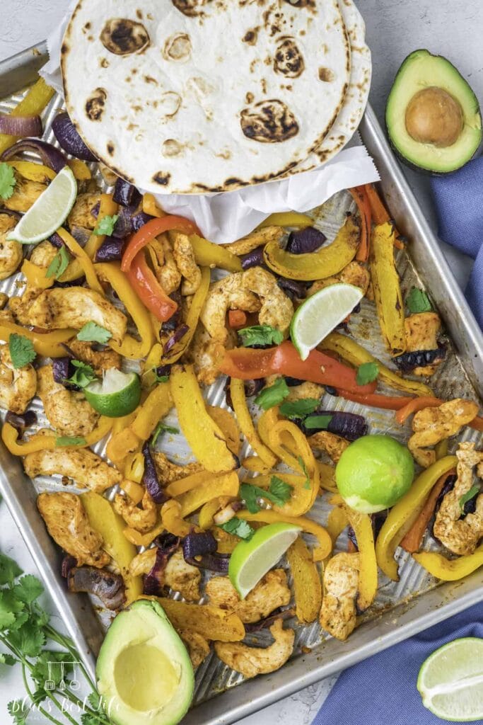 Sheet Pan Chicken Fajitas on a baking sheet with tortillas and lime wedges.