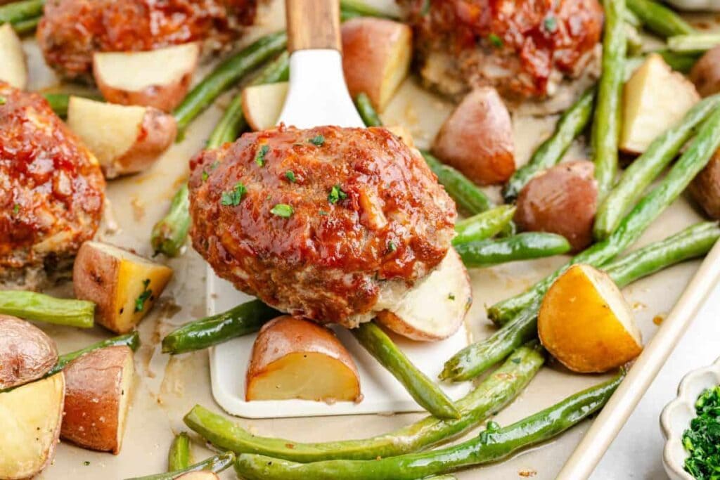 Mini meatloaf on a spatula with roasted vegetables.