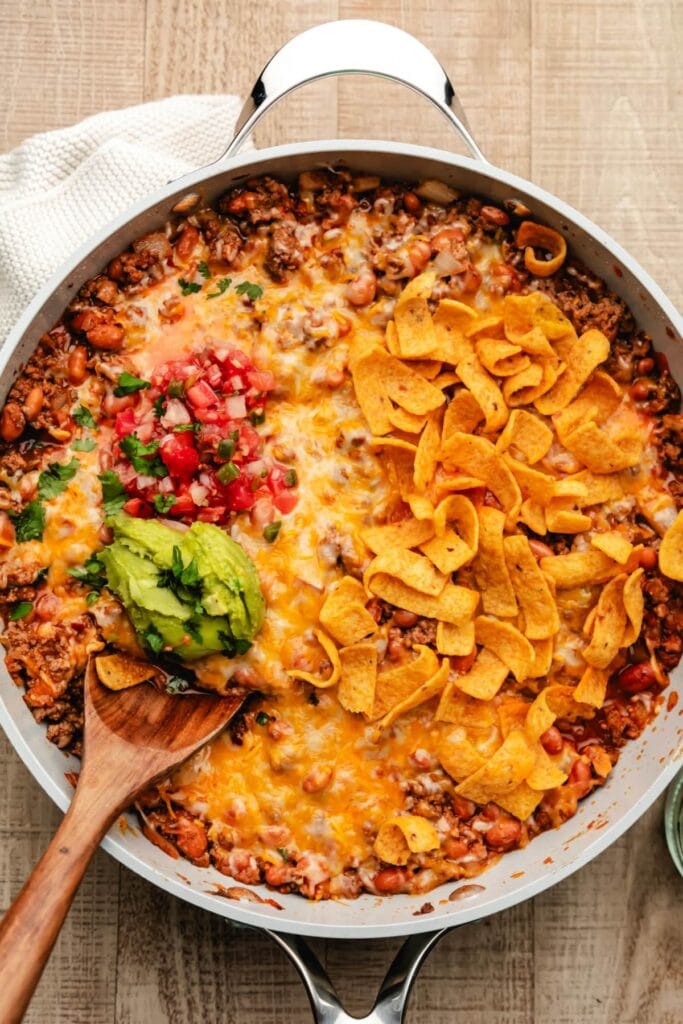 Overhead view of taco skillet topped with cheese, avocado, salsa, and corn chips.
