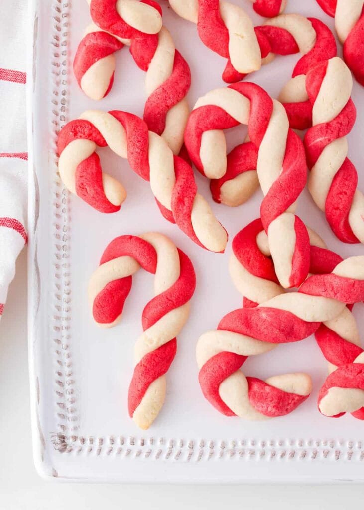 White plate of red-and-white twisted candy cane cookies, neatly arranged with striped cloth beside.