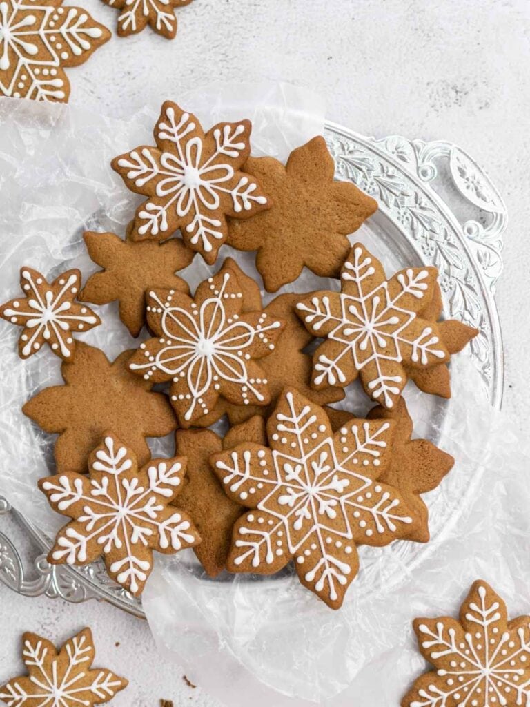 Snowflake-shaped gingerbread cookies decorated with intricate white icing, arranged on silver tray lined with parchment paper.