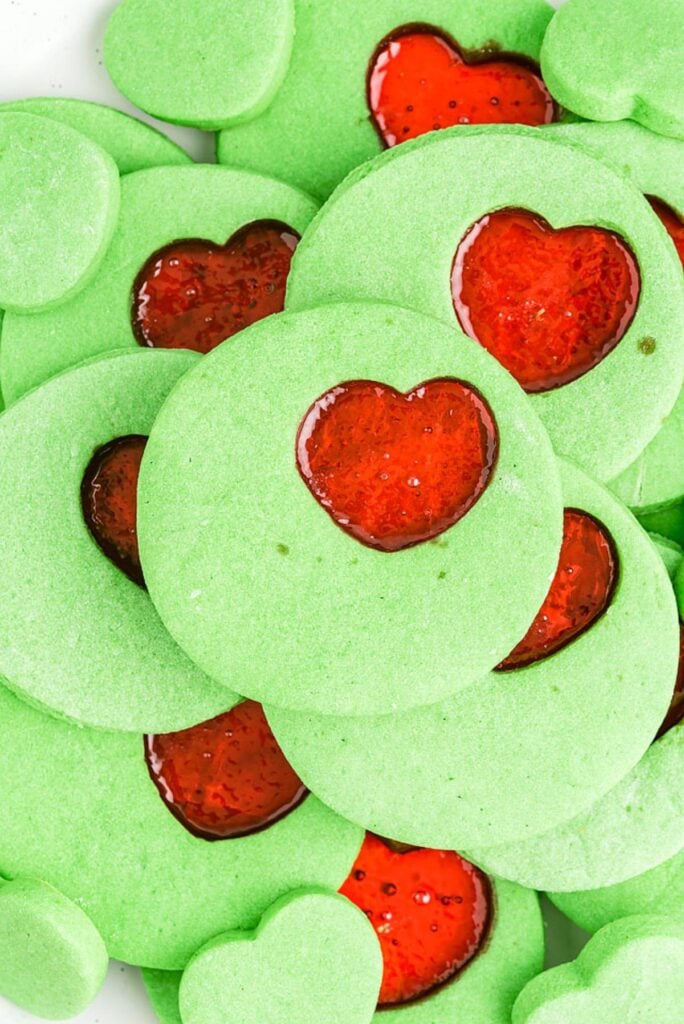Round green cookies with red heart-shaped jam centers, close-up view highlighting vibrant contrast.