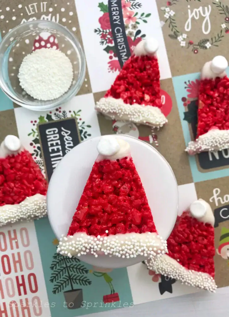 Red Rice Krispies triangles decorated as Santa hats with white frosting trim, sprinkles, and pom-pom tops, arranged on festive background with Christmas text.