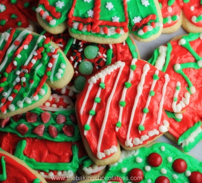 Colorful Christmas sweater cookies decorated with red, green, and white icing, sprinkles, and festive patterns, arranged closely on pink background.